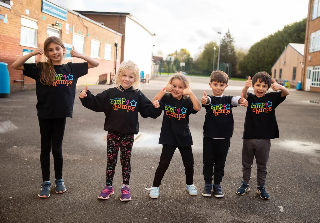 Children wearing Camp 4 Champs T-shirts and giving thumbs up outside camp